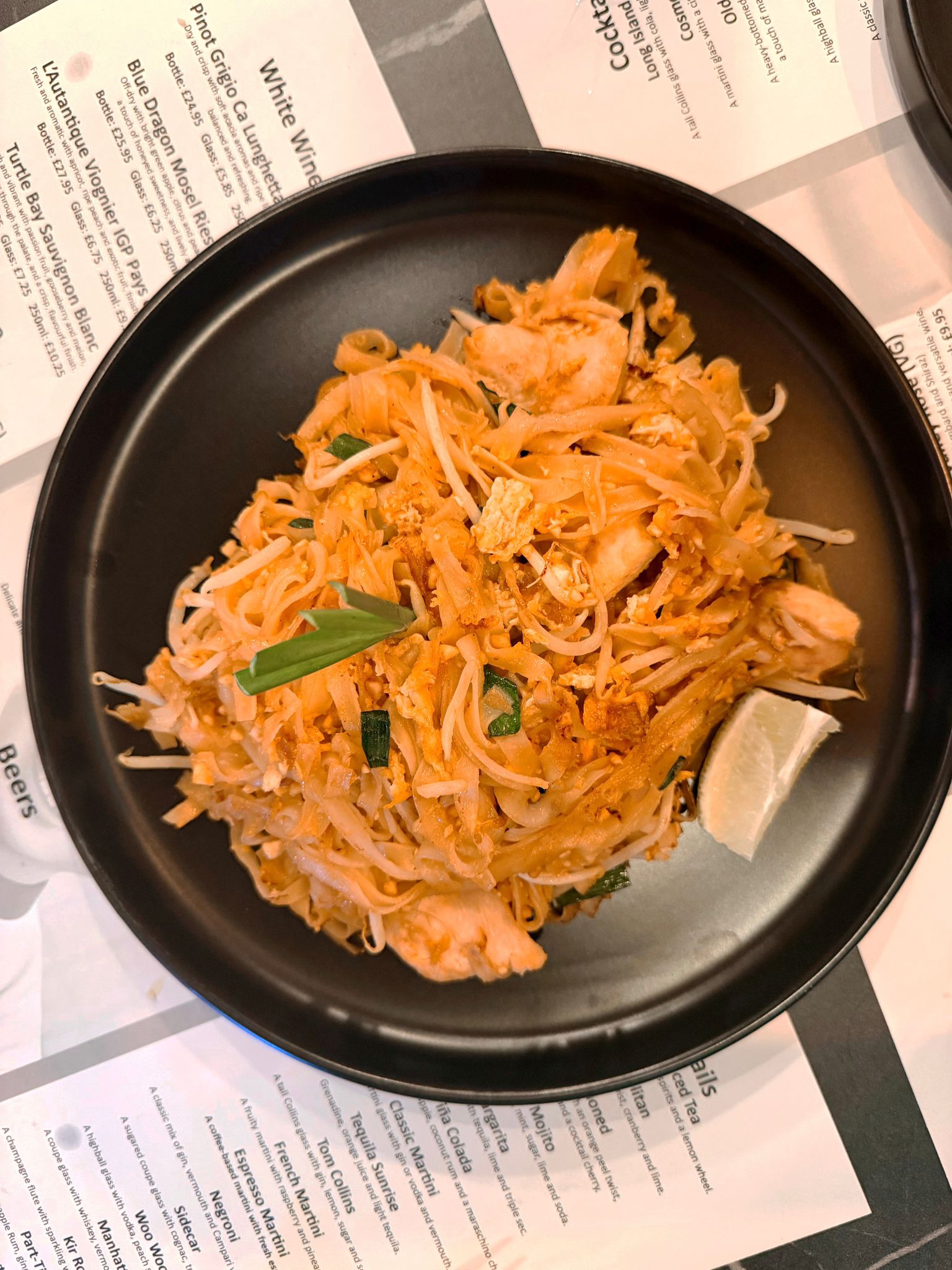 Tata's chicken Pad Thai on a black plate over the printed menu